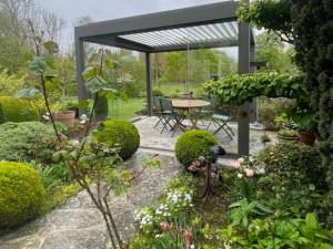 Pergola anthracite lames, table ronde et chaises vertes dans jardin buise