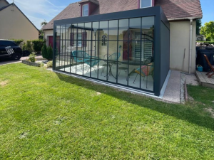 Extension vitrée croisillons noirs, salon coloré et toiture tuiles brunes
