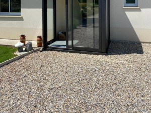 Sas vitre anthracite sur gravier devant facade beige, pots terre cuite et decor jardin