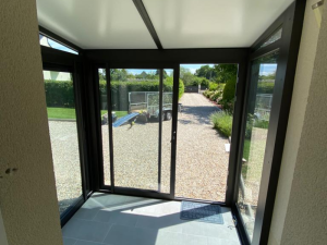 Interieur sas alu noir, carrelage gris clair et baie coulissante ouvrant sur gravier