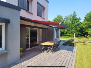 Store banne rouge vif sur terrasse bois grise devant facade moderne