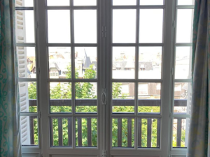 Fenêtre blanche petits bois vue balcon, toits colombages et rideaux imprimés