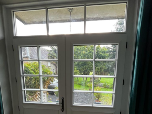 Porte-fenêtre double blanche petits bois, imposte et vue jardin depuis pièce