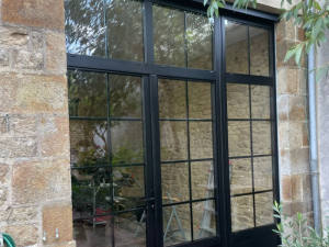 Baie vitree style atelier noire petits bois sur mur pierre apparente
