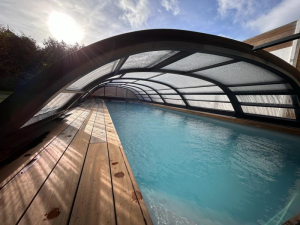 Abri piscine bas galbe anthracite, reflets soleil sur plage bois