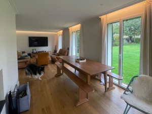 Trois portes-fenetres blanches sur jardin, table bois massif et salons cuir dans piece lumineuse