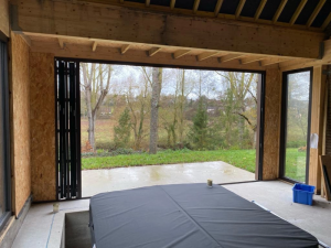 Baie pliante noire repliee dans extension bois OSB, spa encastre au sol et vue jardin