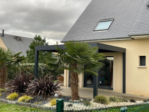 Pergola anthracite adossee maison beige, palmiers et paillage pierres