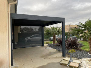 Pergola anthracite, store lateral gris sur dalle beton et massif paysage
