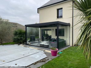 Pergola veranda anthracite, baies vitrees et pelouse verte sous ciel gris
