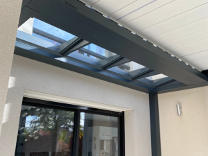 Gros plan pergola Brustor, lames blanches et vitrage sous baie anthracite