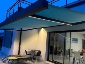 Store banne turquoise LED au crepuscule, table bistro et transats sur terrasse carrelee