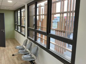 Salle d'attente, fenetres anthracite et brise-soleil bois, chaises metal perfore