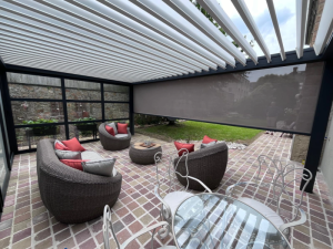 Pergola anthracite, screen lateral gris et fauteuils rotin arrondis sur terrasse paves