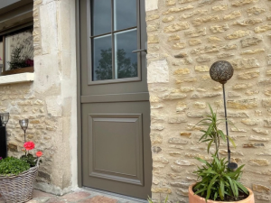 Porte entree taupe quatre vitraux, encadrement pierre et geraniums rouges en panier