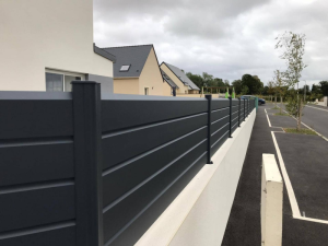 Clôture anthracite sur muret blanc le long trottoir, maisons et rue résidentielle