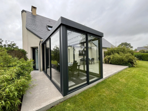 Veranda grise toit plat vitrages, terrasse beton maison ardoise et pelouse