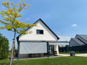 Pergola noire, toile rétractable et stores verticaux blancs sur terrasse maison blanche