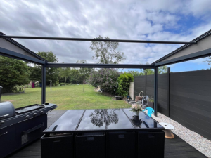 Terrasse anthracite, table verre, clôture lames et pelouse sous pergola