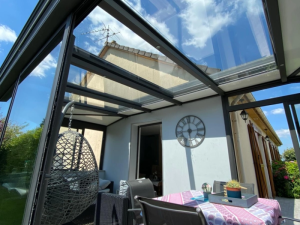 Interieur veranda toit vitre, fauteuil suspendu, salon et horloge murale