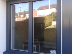 Fenêtre double anthracite en gros plan, reflets quartier sur façade crème