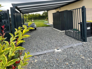 Carport anthracite toit rayé, remorque sous abri et cabanon le long façade beige