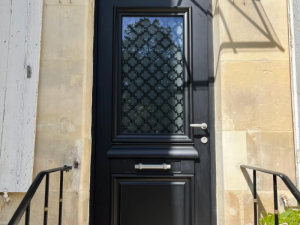Porte entree noire mate, vitrail grille fleurs de lys sur mur pierre claire