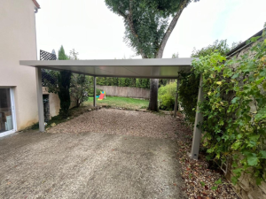 Carport toit plat adossé à une maison, mur pierre couvert de lierre et pelouse