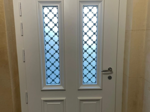 Porte entree blanche, deux vitrages depolis grilles noires, mur pierre