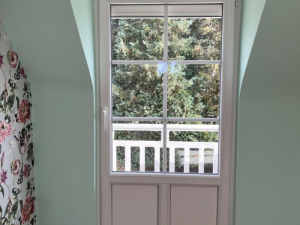 Porte-fenêtre blanche petits bois en mansarde, balcon blanc et thuyas verts