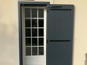 Porte vitree petits bois blanche, volet battant anthracite ouvert sur crepi beige