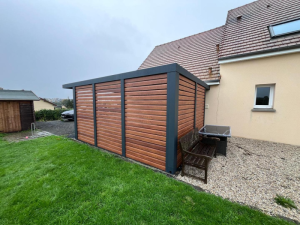 Abri alu anthracite lames bois horizontales adossé, gravier et tondeuse devant