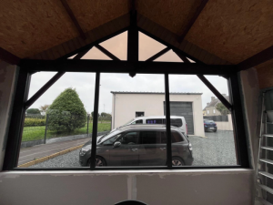 Fenetre pignon noir avec treillis bois, chantier placo et cour gravier avec voitures