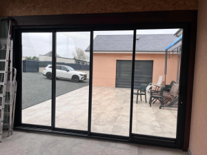 Baie coulissante trois vantaux noir, vue terrasse carrelée et voiture blanche dehors
