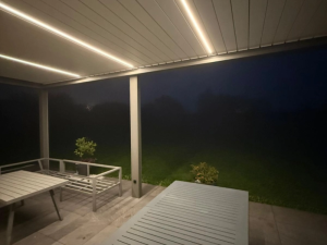 Pergola grise de nuit, rubans LED au plafond et table metal sur terrasse