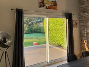 Interieur baie coulissante blanche, vue terrasse pelouse et tondeuse robot
