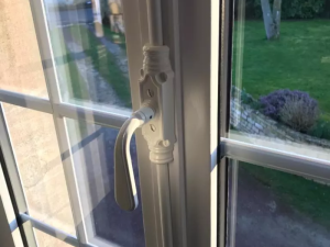 Gros plan poignée crémone blanche sur fenêtre petits bois, jardin en fond