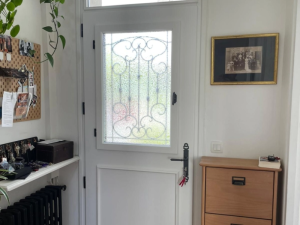 Porte d'entrée blanche semi-vitrée, grille fer forgé noire et poignée longue, hall