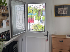 Porte blanche, imposte vitrée ouverte avec grille forgée, vue portail rouge et jardin