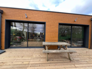 Double baie coulissante anthracite sur bardage bois, terrasse et sapin de Noël