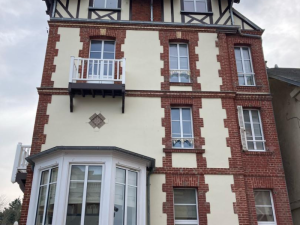 Façade briques rouges et crépi, fenêtres blanches, bow-window et balcon barreaux