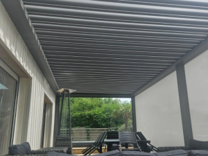 Sous pergola grise, lames orientables fermées, salon rotin et table à manger noire