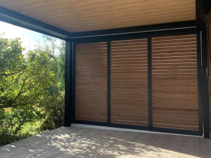 Pergola noire, parois coulissantes lames bois sur terrasse carrelée claire