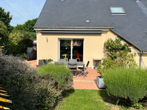 Façade crépi beige, store banne anthracite rétracté au-dessus d'une baie vitrée blanche