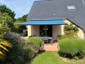 Store banne coffre bleu déployé ombrageant table grise sur terrasse carrelée terracotta