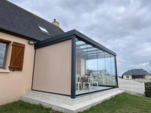 Véranda anthracite vitrée toit plat sur terrasse carrelée devant maison crépi saumon