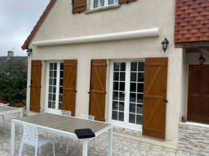 Store banne coffre blanc, volets bois marron et portes-fenêtres blanches sur terrasse