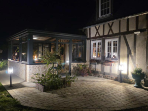 Véranda éclairée la nuit sur colombages, terrasse pavée et lampes sur pied noires