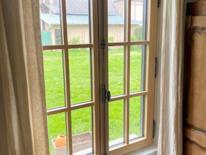 Fenêtre bois clair double vantail à petits bois, crémone noire et rideaux beige