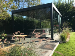 Abri spa anthracite parois vitrées sur terrasse bois, herbes ornementales au premier plan